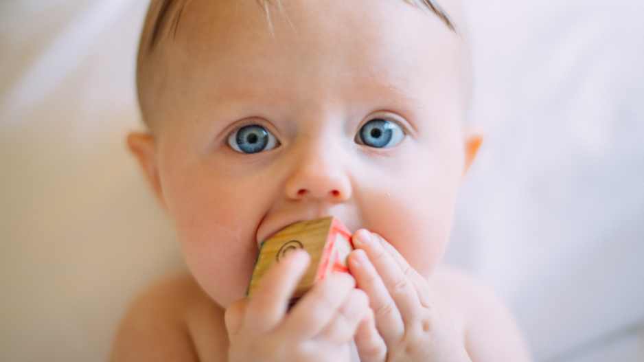 baby-kaut-an-spielwuerfel Baby mit blauen Augen kaut gedankenverloren an einem Spielwürfel